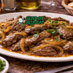 Fegato alla Veneziana disajikan hangat di piring putih dengan irisan hati sapi muda lembut, bawang bombai creamy, taburan peterseli, dan polenta panggang di sampingnya