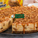 Cheesecake berlapis krim dengan topping karamel dan remah biskuit renyah berwarna keemasan
