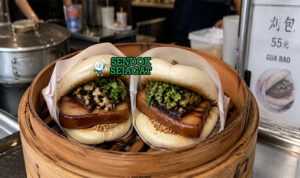 Roti kukus putih lembut terlipat dengan isian daging babi berwarna cokelat karamel, kacang tumbuk, dan daun ketumbar segar