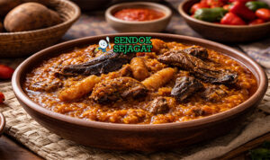 Ikokore khas Nigeria dengan porridge ubi kental berwarna oranye dari palm oil, potongan ikan asap, ponmo, dan daun efirin disajikan di mangkuk