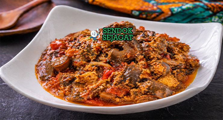 Mangkuk isi ewu khas Nigeria dengan potongan kepala kambing empuk, saus minyak sawit merah kental, taburan bawang bombay dan daun utazi segar