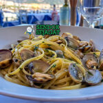 Pasta linguine dengan kerang bercangkang terbuka, minyak zaitun berkilau, taburan parsley hijau, dan tampilan elegan sederhana