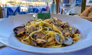 Pasta linguine dengan kerang bercangkang terbuka, minyak zaitun berkilau, taburan parsley hijau, dan tampilan elegan sederhana