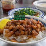 Semangkuk nasi putih hangat dengan topping daging babi cincang berkuah cokelat pekat dan telur rebus kecap yang mengilap