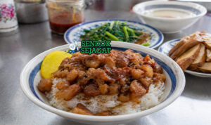 Semangkuk nasi putih hangat dengan topping daging babi cincang berkuah cokelat pekat dan telur rebus kecap yang mengilap
