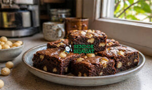 Brownies cokelat pekat dengan tekstur fudgy dan potongan kacang macadamia renyah di permukaan