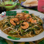 Semangkuk mie kangkung Betawi berkuah cokelat kental, mie kuning, kangkung hijau segar, tauge renyah, dan udang yang menggoda selera