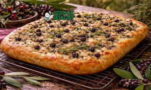 Native pepperberry focaccia disajikan hangat di piring kayu dengan permukaan keemasan berlubang-lubang, taburan sea salt flakes dan bubuk pepperberry yang harum