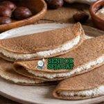 Pancake tipis berwarna cokelat dari tepung kastanye dengan isian ricotta putih lembut di atas piring rustic