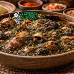 Okazi soup khas Nigeria dengan kuah kental berwarna oranye, berisi daging, ikan, dan daun okazi hijau, disajikan hangat di mangkuk