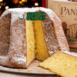 Kue pandoro berbentuk bintang berwarna keemasan dengan tekstur lembut, ditaburi gula halus putih seperti salju, tampilan elegan khas Italia