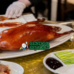 Peking duck khas Beijing dengan kulit cokelat keemasan mengkilap, tampak renyah dengan potongan tipis daging juicy, disajikan bersama pancake tipis, saus hoisin, dan irisan daun bawang
