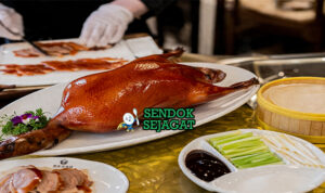 Peking duck khas Beijing dengan kulit cokelat keemasan mengkilap, tampak renyah dengan potongan tipis daging juicy, disajikan bersama pancake tipis, saus hoisin, dan irisan daun bawang