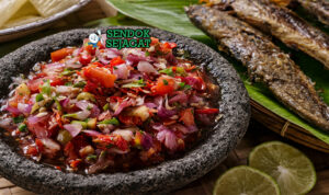 Sambal colo-colo khas Maluku dengan cabai, bawang, tomat, dan terasi yang ditumbuk kasar, disajikan segar di cobek bersama ikan bakar