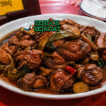 Potongan ayam berwarna cokelat gelap mengilap dengan saus kental, bawang putih, jahe, dan daun basil segar