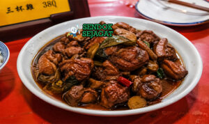 Potongan ayam berwarna cokelat gelap mengilap dengan saus kental, bawang putih, jahe, dan daun basil segar