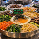 Mangkuk sanchae bibimbap khas Korea dengan nasi hangat, aneka sayuran gunung seperti bayam dan gosari, telur mata sapi, dan saus gochujang merah menggoda