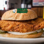 Sandwich dengan daging tenderloin goreng berukuran besar, roti bun, selada segar, dan saus creamy yang menggoda