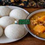 Sajian tuwo shinkafa berbentuk bulat putih lembut dengan tekstur halus, disajikan bersama sup sayur berwarna merah kehijauan khas Nigeria