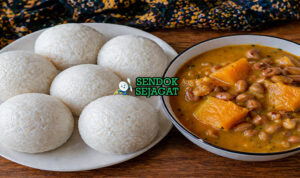 Sajian tuwo shinkafa berbentuk bulat putih lembut dengan tekstur halus, disajikan bersama sup sayur berwarna merah kehijauan khas Nigeria