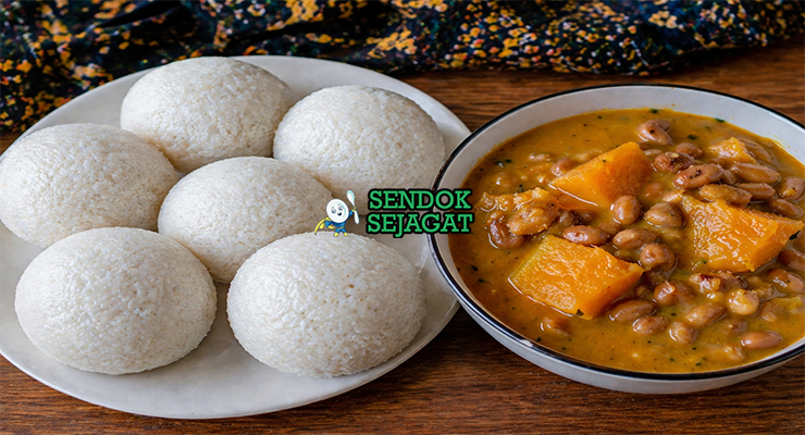 Sajian tuwo shinkafa berbentuk bulat putih lembut dengan tekstur halus, disajikan bersama sup sayur berwarna merah kehijauan khas Nigeria